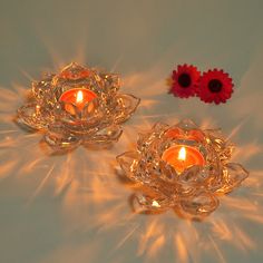 two lit candles sitting next to each other on a white surface with red flowers in the background