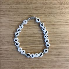 a white beaded bracelet with words written in black and white letters on it, sitting on a wooden surface