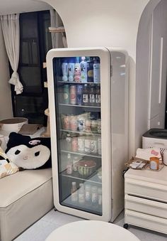 the refrigerator is full of drinks and other items in this small room with white furniture