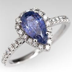 This beautiful sapphire engagement ring is centered with one (1) pear cut no heat Madagascar origin sapphire weighing 1.20 carats and set with four-prongs. The sapphire is bordered with seventeen (17), prong set, round brilliant cut diamonds. The top face of the shank is accented with a eight (8), prong set, round brilliant cut diamonds on each side. The ring measures 11.7mm at the top, rises 6.4mm above the finger, tapering to 1.6mm wide and 1.2mm thick at the base of the shank. The ring is cur Teardrop Sapphire Ring With Diamond And Prong Setting, Pear-shaped Sapphire Ring, Elegant Teardrop Sapphire Ring With Center Stone, Formal Teardrop Sapphire Ring With Prong Setting, Formal Pear-shaped Sapphire Ring With Vvs Clarity, Fine Jewelry Sapphire Teardrop Ring With Prong Setting, Elegant Pear-shaped Sapphire Ring For Formal Occasions, Fine Jewelry Sapphire Ring With Teardrop Prong Setting, Formal Pear-shaped Sapphire Ring