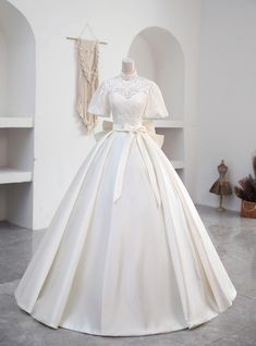 Laced with the nostalgia of a bygone era, this wedding dress boasts a high-neck lace bodice that radiates elegance and poise. Its delicate sleeves brush the edges of the shoulders, a soft prelude to the voluminous satin skirt that cascades into a regal train. The simplicity of the silhouette is its grandeur, tied together by a satin sash at the waist, making this gown a timeless choice for a bride's unforgettable day. Wedding Dresses With Neck Collar, Elegant Cream Lace Ball Gown, Cream Lace Ball Gown For Wedding, White Lace Ball Gown With Lace Trim, Lace Gown With Lace Trim For Debutante Ball, Lace Ball Gown Wedding Dress With Lace Trim, White Lace Ball Gown With Lace Bodice, Wedding Dress With Lace Trim For Debutante Ball, Lace Wedding Ball Gown With Lace Back