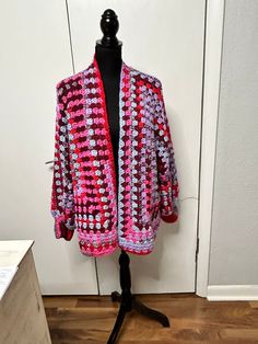 a crocheted pink and white jacket sitting on top of a mannequin