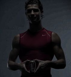 a man holding a can of beer in his hands while wearing a red shirt and black shorts