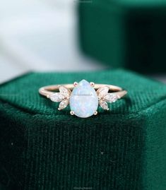 a white opal and diamond ring sitting on top of a green box