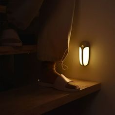 a person standing next to a light that is on top of a wooden shelf in a dark room