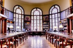 an empty library with tables and chairs in front of two large stained glass windowed windows