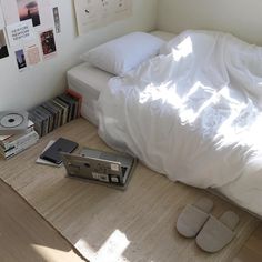 there is a bed with white sheets and books on the floor next to an mp3 player