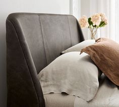 a close up of a bed with pillows and a vase on the back of it