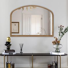 there is a mirror on the wall above a table with books and vases next to it