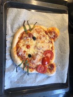 a pizza with tomatoes, olives and cheese on it sitting on a baking sheet