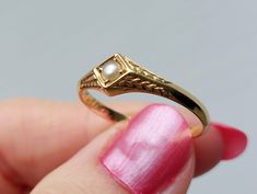 a woman's hand holding a gold ring with a pearl in the middle,