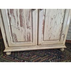 an old white cabinet with peeling paint on the top and bottom, sitting on a rug in front of a brick wall