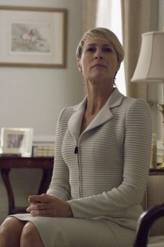 a woman sitting on a chair in a living room next to a table and lamp