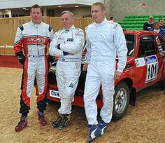 three men in racing suits standing next to a red car