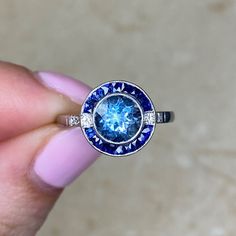 a woman's hand holding a ring with a blue diamond in the center and white diamonds around it