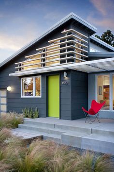 a red chair sitting in front of a gray house with green door and window sill