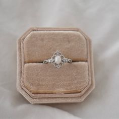 an engagement ring in a velvet box on a white cloth covered tablecloth, with the diamond set at the center