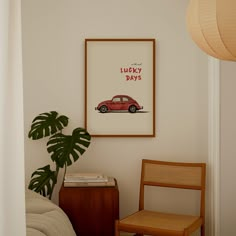 a red car is hanging on the wall next to a wooden chair and table with a plant