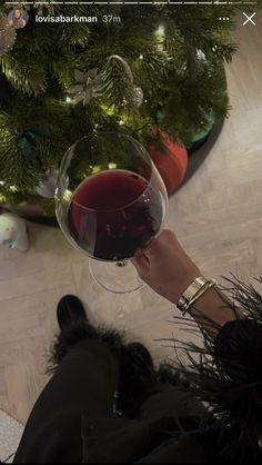 a person holding a wine glass in front of a christmas tree