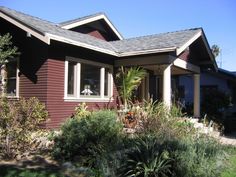 a house that is red and brown with some plants in front of the house,