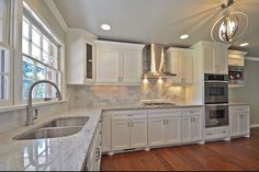 a kitchen with white cabinets and marble counter tops