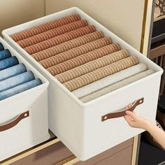 two white storage bins filled with towels and blankets on top of a dresser next to a hand reaching for one