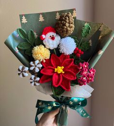 a person holding a bouquet of flowers with pine cones on top and other holiday decorations