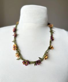 This necklace features a delicate braided This is a delicate necklace handcrafted with silk thread, featuring intricately crocheted flowers in shades of purple, yellow, and green. The floral elements are connected by a green silk thread that resembles vines, creating a natural and elegant look. Crocheted Flowers, Lace Necklace, Needle Lace, Floral Elements, Necklace Unique, Handcrafted Necklace, Yellow And Green, Green Silk, Silk Thread