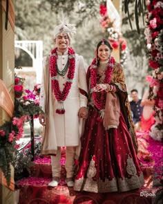 two people standing next to each other in front of flowers and garlands on the ground