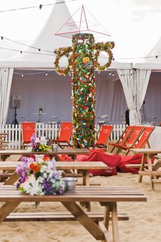 a cross made out of christmas lights is on the beach with red chairs and tables