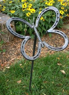 a metal butterfly sculpture sitting on top of a green grass covered field next to yellow flowers