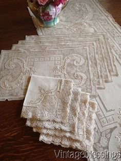 several white doily on a wooden table with flowers in a vase and two napkins