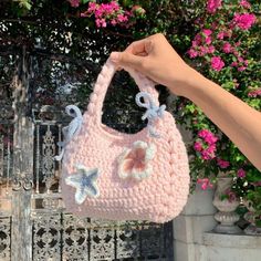 a hand holding a pink crocheted purse with starfish decorations on the handle