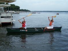 two people in a canoe with paddles on the water and boats docked behind them