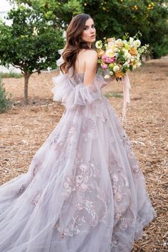 a woman in a wedding dress holding a bouquet and looking off into the distance with an orange tree behind her