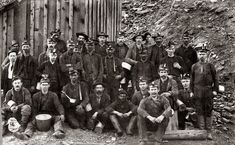 a group of men standing next to each other in front of a wooden fence and building