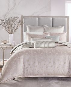 a bed with white and grey comforters in a bedroom next to a vase filled with flowers