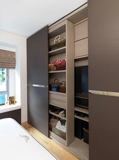 a bed sitting under a window next to a wooden shelf filled with baskets and bags