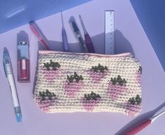 a crocheted purse with pens and pencils next to it