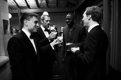 several men in suits and ties standing around drinking wine from champagne glasses while another man looks on