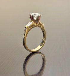 a gold ring with a princess cut diamond in the center on a reflective table top