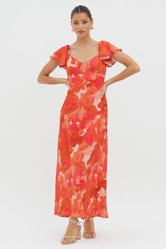 a woman in an orange floral print dress with ruffle sleeves and open shoulders, posing for the camera