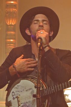 a man with a hat on singing into a microphone and holding a guitar in front of him