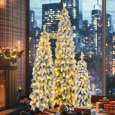 two white christmas trees in front of a large window with city lights and presents on the floor