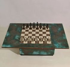 a metal chess set sitting on top of a green table next to a white wall