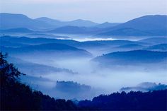 the mountains are covered in fog and low lying clouds at dusk or dawn as seen from an overlook point