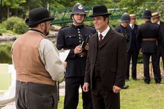 two men in top hats are talking to each other while others stand near the water