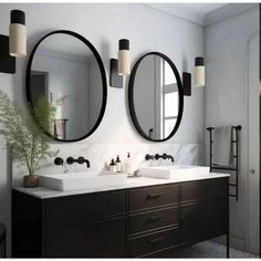 two round mirrors are above the double sinks in this bathroom with black cabinets and white countertops