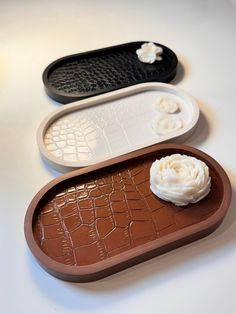 three trays with different designs on them sitting on a white counter top, one has a flower in the center