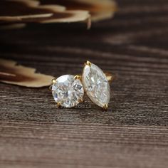 two pear shaped diamond studs sitting on top of a wooden table next to feathers